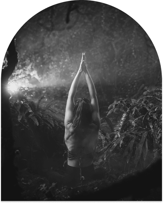 Marylou Forges, de dos, en posture d'élévation des bras dans une forêt brumeuse, avec des rayons de lumière filtrant à travers la végétation.
