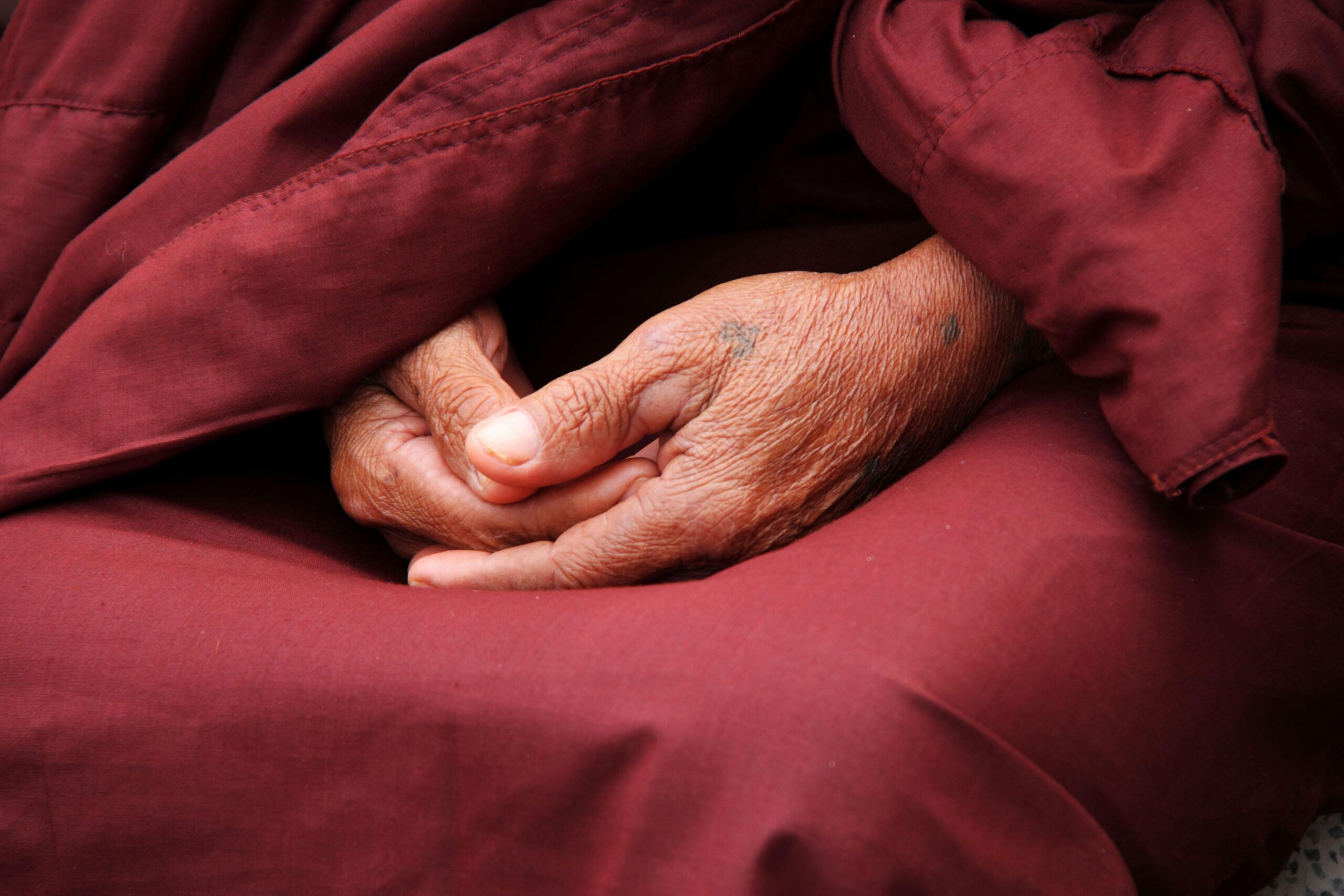 Mains en Dhyana Mudra, posées l’une sur l’autre sous une étoffe rouge, geste de méditation et de sérénité.