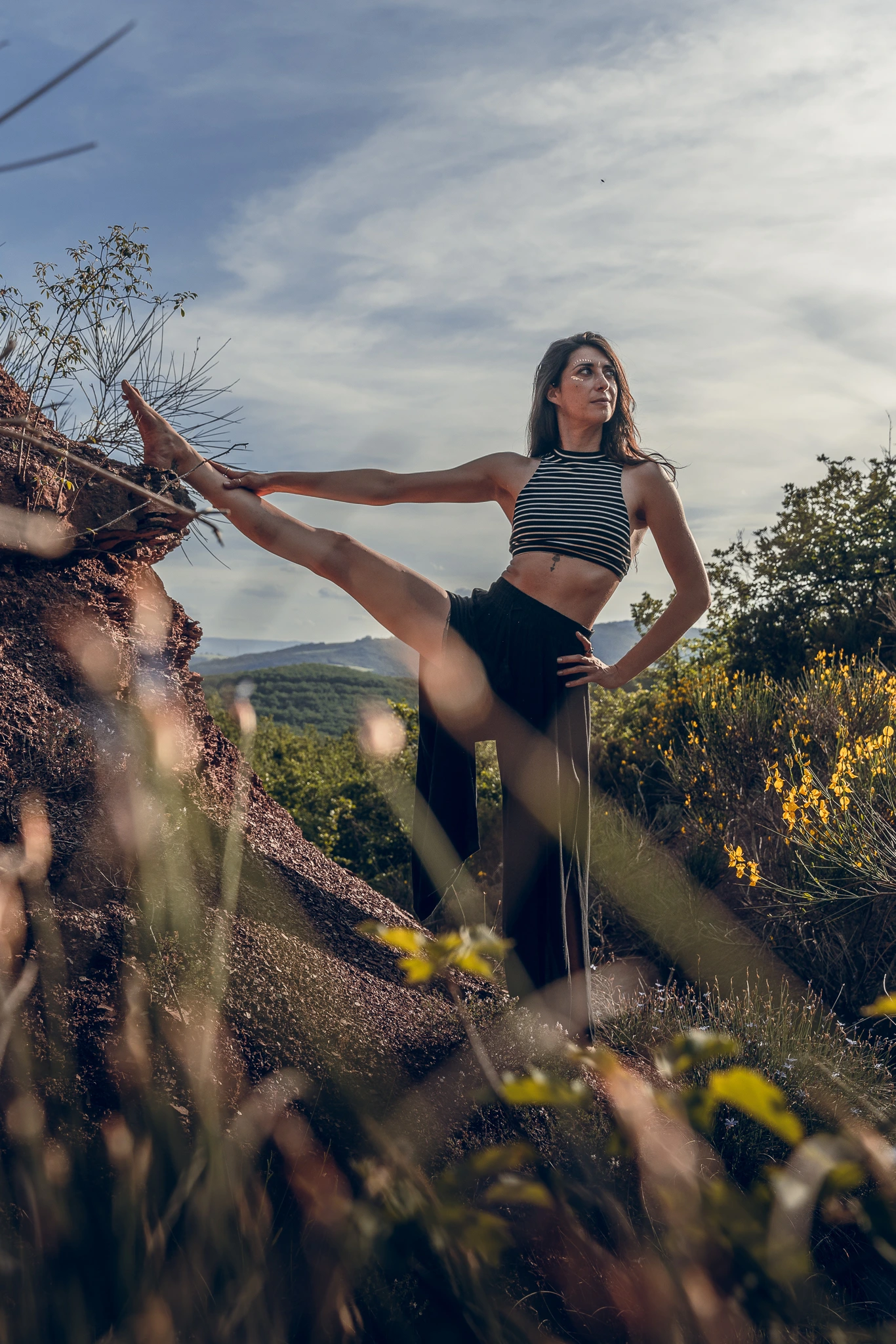 Marylou Forges, fondatrice de Yoga Le Refuge à Saint-Rome-de-Tarn, en posture jambe levée latéralement sur un rocher rouge dans l’Aveyron
