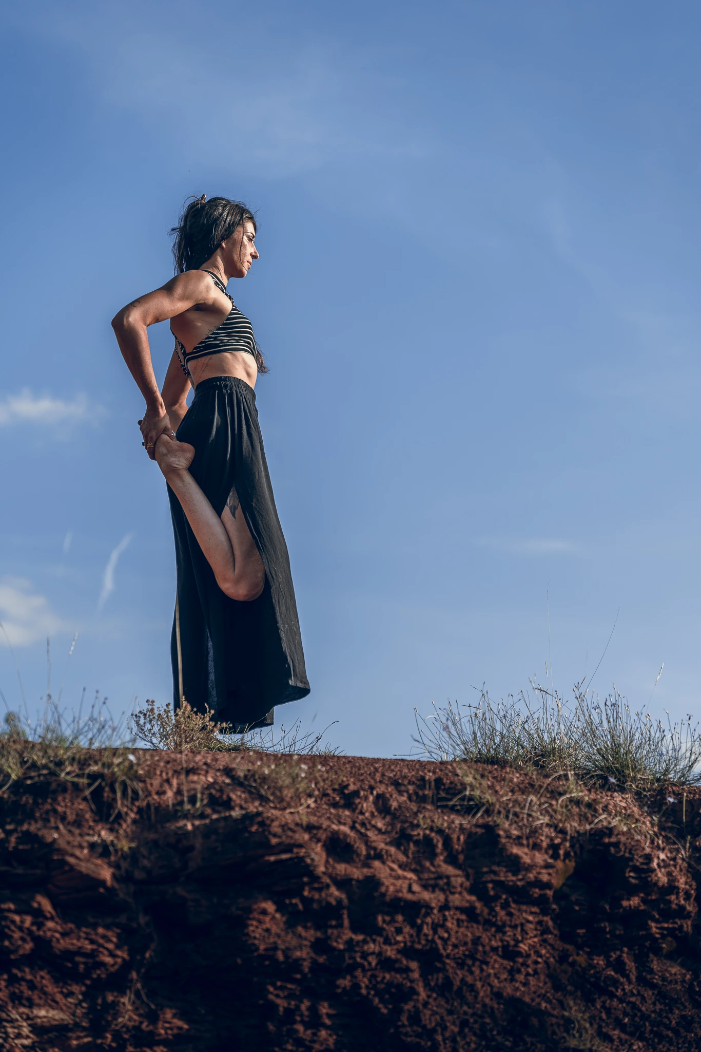 Marylou Forges, professeure de yoga et fondatrice de Yoga Le Refuge à Saint-Rome-de-Tarn, réalisant une posture d’équilibre debout sur un rocher rouge sous un ciel bleu dans l’Aveyron