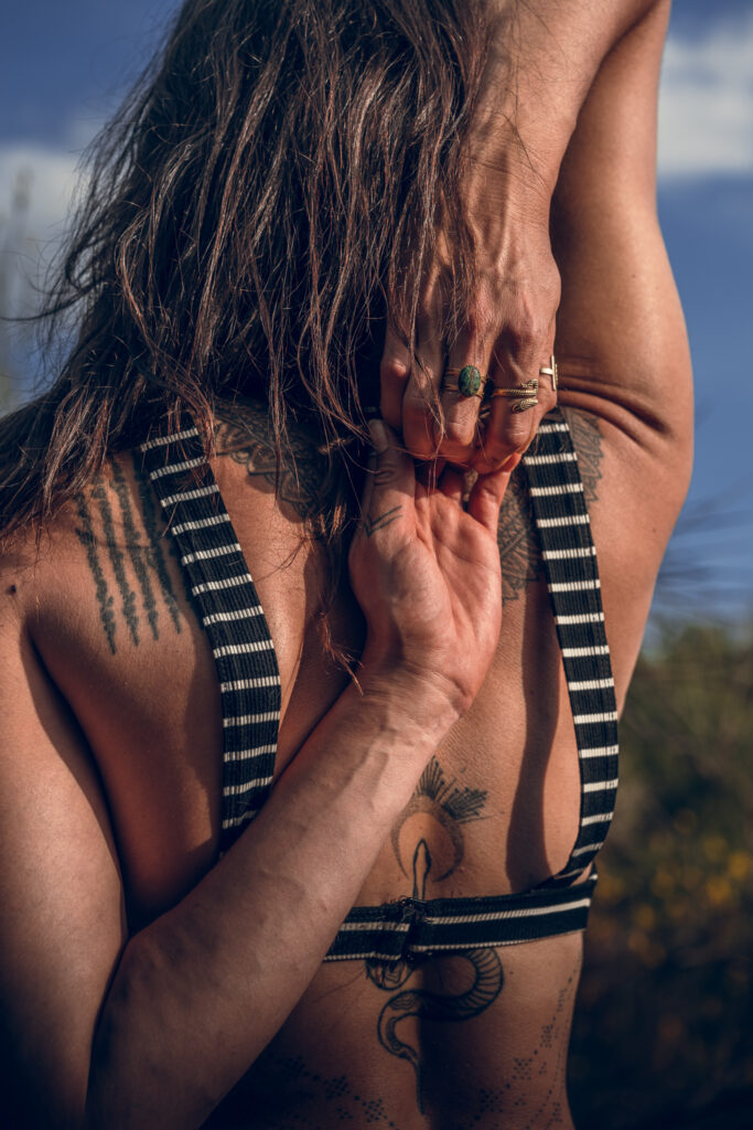 Marylou Forges en posture de yoga Gomukhasana (bras liés derrière le dos), mettant en valeur la souplesse des épaules et l’ancrage, avec tatouages spirituels visibles.