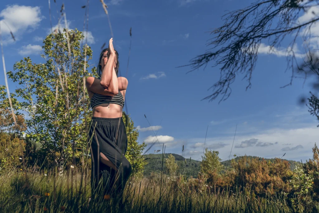 Marylou Forges, fondatrice de Yoga Le Refuge à Saint-Rome-de-Tarn, en posture de l’aigle dans un champ ensoleillé avec vue sur les collines de l’Aveyron