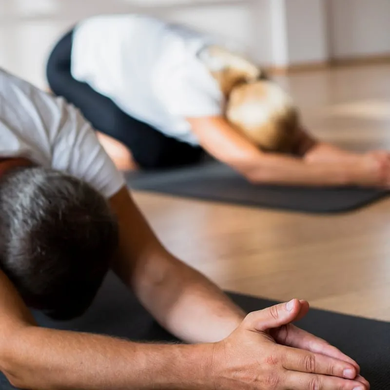 Participants seniors en posture de l’enfant lors d’un cours de yoga en salle avec Marylou Forges, fondatrice de Yoga Le Refuge à Saint-Rome-de-Tarn