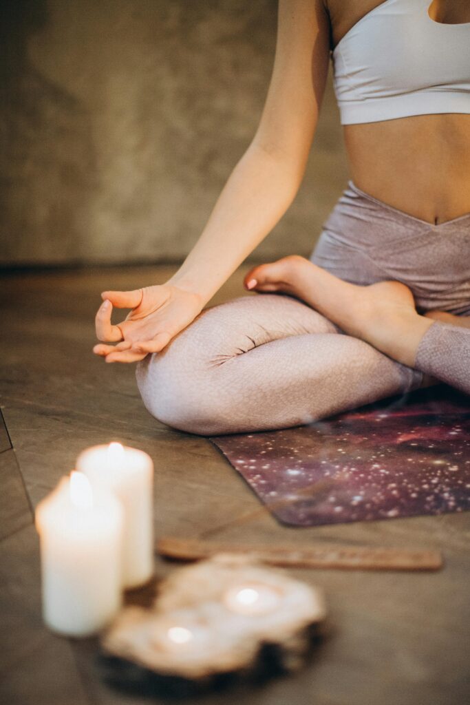 Jambes d’une femme en Padmasana, posture du lotus, avec les mains en Jnana Mudra devant des bougies, pratique de méditation et de yoga.