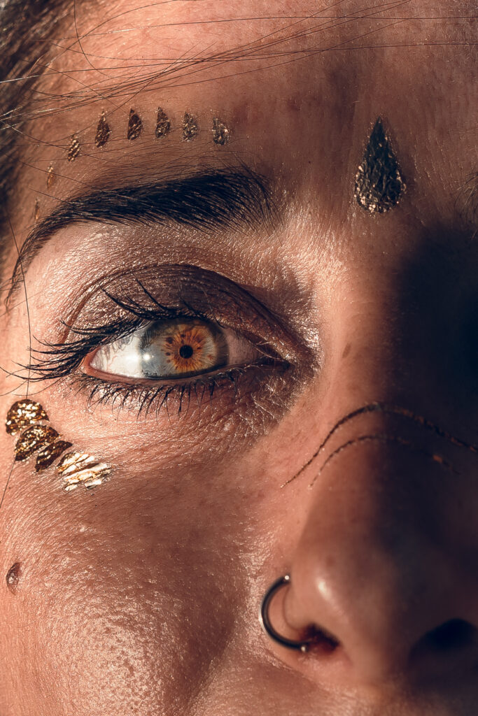 Gros plan sur un visage orné de dorures évoquant le chakra du troisième œil (Ajna), symbole d’intuition, de clarté et de vision intérieure.