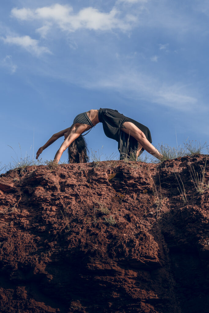 Femme pratiquant une posture de yoga en pont dans le Rougier sous un ciel bleu.